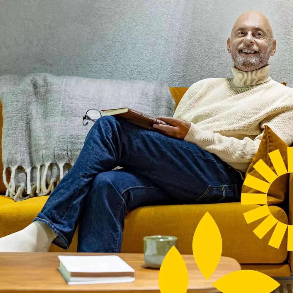 Tyylikkäästi ikääntynyt mies istuu kirja kädessä sohvalla