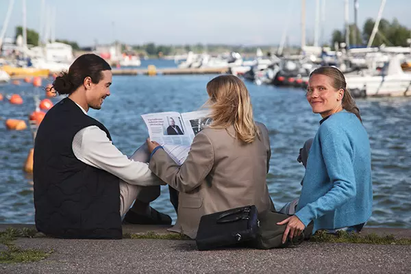 Kolme henkilöä istuu veneiden äärellä
