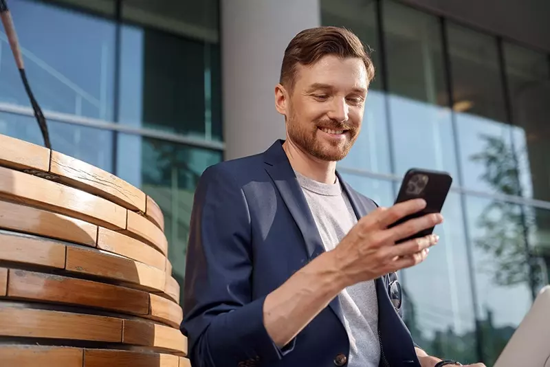 Mies katsoo puhelinta lasiseinäisen talon edessä