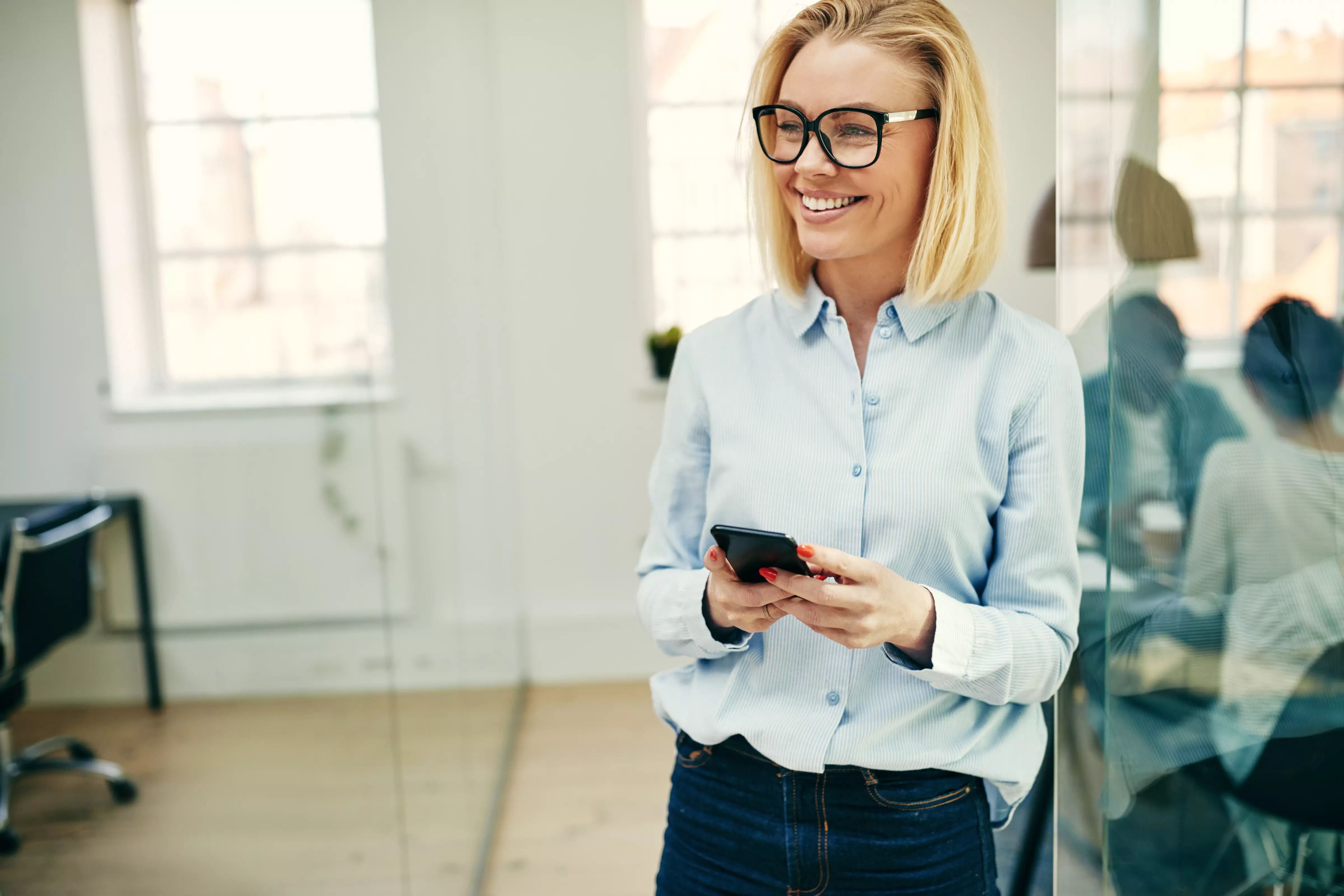 Kuva, jossa nainen katsoo puhelinta toimistolla