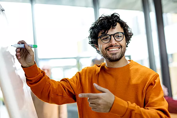 A man smiles while writing with a marker on the whiteboard