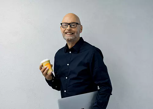 Mies hymyilee kahvimuki kädessä