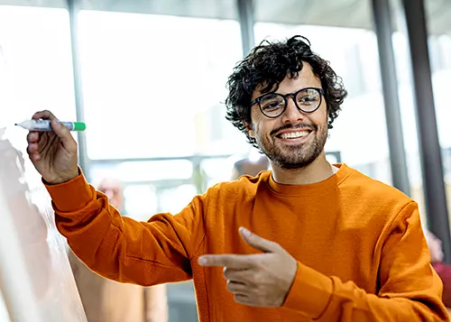 A man is smiling at a whiteboard with a marker in his hand