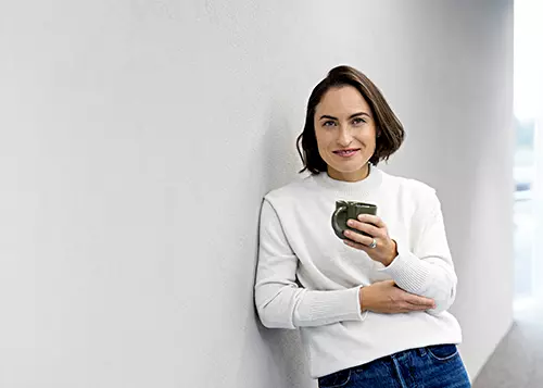 Nainen hymyilee kahvikuppi kädessään