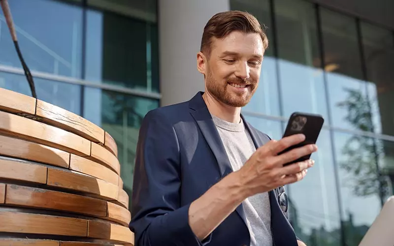 Mies katsoo mobiililaitetta modernin toimistorakennuksen edessä