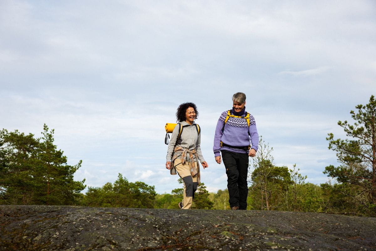 Kaksi retkeilijää kävelemässä kalliolla taustana metsää ja pilvinen taivas