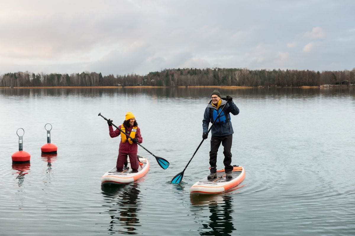 Kaksi henkilöä meloo SUP-laudoilla syksyisellä järvellä. Taustalla metsää.
