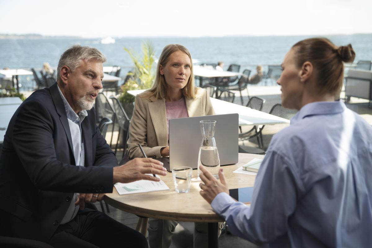 Kolme henkilöä keskustelee pöydän ääressä terassilla