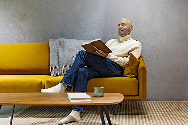 An elderly man is sitting on the sofa with a book in his lap