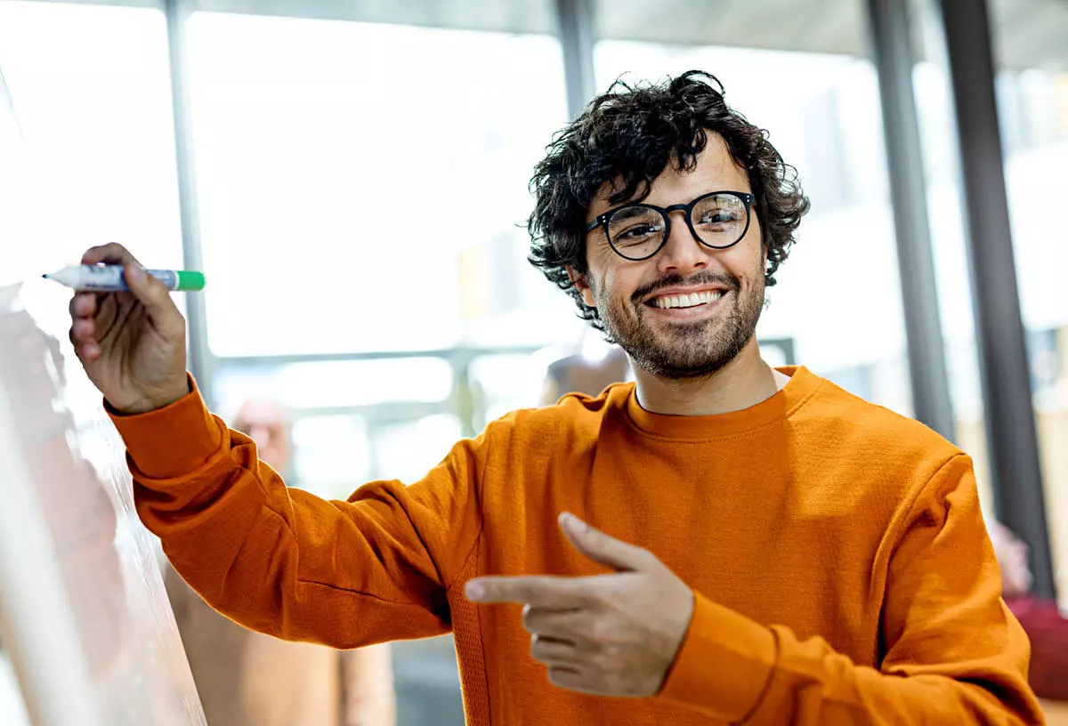 Hymyilevä mies kirjoittaa valkotaululle