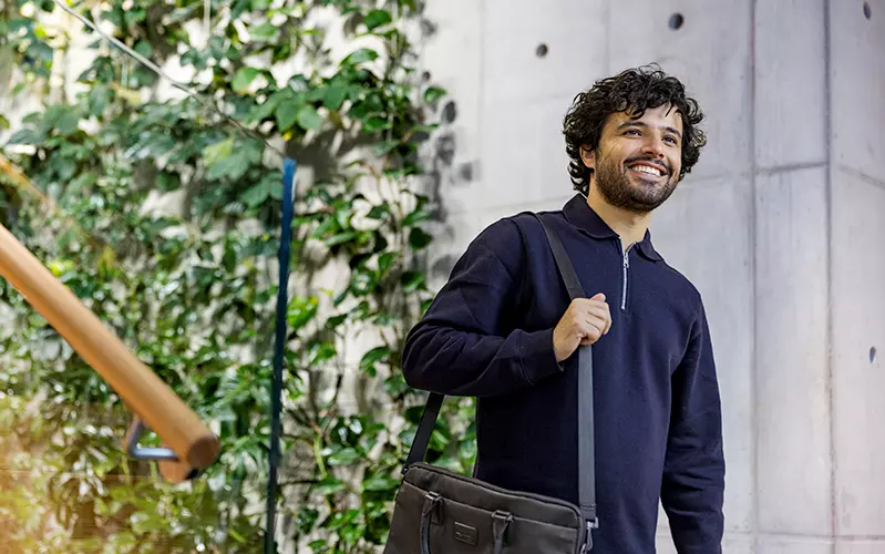A man is walking in an office with a bag on his shoulder