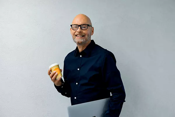 A man smiles with a coffee mug in his hand